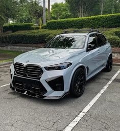 the new bmw x5 suv is parked in a parking lot with trees and bushes behind it