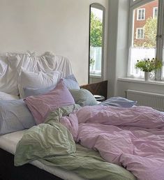 an unmade bed with several pillows and blankets on it in front of a window