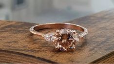 an oval shaped diamond ring with three pear shaped diamonds on the band, sitting on top of a wooden surface