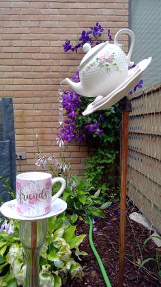 there is a tea pot on top of a stand next to some flowers and plants