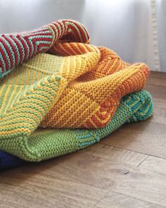 a pile of colorful knitted blankets sitting on top of a wooden floor