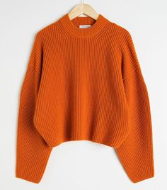 an orange sweater hanging on a hanger with the top half turned to show it's long sleeves