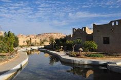 a river running through a small village next to a desert like area with buildings and trees