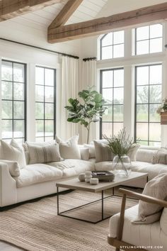 a living room filled with white furniture and large windows in the wall behind it is a couch, chair, coffee table, and potted plant