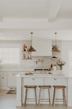 a kitchen with two stools and an island in the middle of it, surrounded by white cabinets