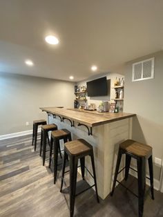 a basement bar with stools and a television mounted on the wall behind it,