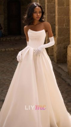 a woman in a white wedding dress standing on a cobblestone street with her hands on her hips