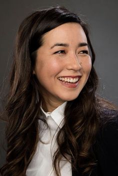 a woman with long dark hair smiling at the camera and wearing a white collared shirt