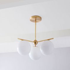 three white balls are hanging from a brass chandelier in an otherwise empty room