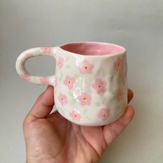 a hand holding a pink and white flowered coffee cup with handles on it's sides