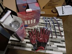 several pairs of red and black gloves sitting on top of a tiled floor next to boxes