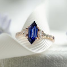 a blue and white diamond ring sitting on top of a white cloth with flowers in the background