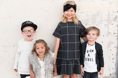 three children standing next to each other in front of a white wall wearing black and white clothing