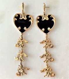 "Antique Gold Tone Hearts & Cupids Drop Pierced Earrings Black Enamel Hand Painted Hearts Hand Set with Faceted Crystal Stones Double Sided Cupids with Wings, Hearts and Bow & Arrows Dangle From the Enamel Hearts Cupids Hearts Hand Set with Faceted Crystal Stones Cupid Dangles are Double Sided with Crystals Hand Set on Both Sides of Hearts Each Earring Hand Set with 10 Crystals Earrings Measure 4 1/2\" Long Black Enamel Hearts Measure 1 1/4\" in Diameter Surgical Steel Posts Silver Tone Gold Enamel Heart Charm Earrings, Gold Enamel Heart-shaped Earrings, Gold Enamel Heart Earrings, Gold Heart-shaped Enamel Earrings, Gold Enamel Heart Earrings For Valentine's Day, Gold Enamel Earrings For Valentine's Day, Elegant Heart-shaped Enamel Earrings, Valentine's Day Gold Heart Enamel Earrings, Black Enamel Jewelry For Wedding