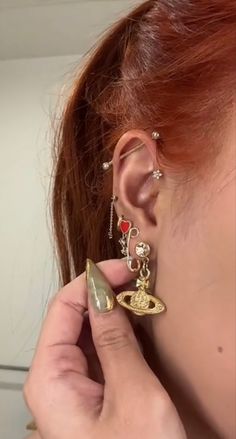 a woman with red hair is wearing gold ear rings and an eye charm on her left ear