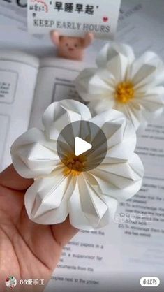 a person is holding some paper flowers in their hand and there are also an open book behind them