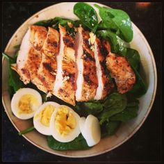 a white plate topped with chicken, hard boiled eggs and spinach