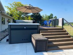 a hot tub sitting on top of a wooden deck next to a patio with an umbrella