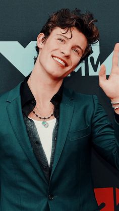 a young man in a green suit making the peace sign with his hand and smiling