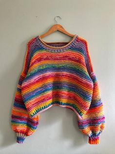 a multicolored sweater hanging on a white wall with a wooden hanger in front of it