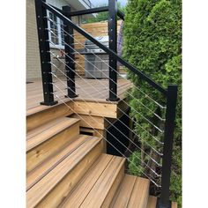 a wooden deck with metal handrails next to a tree and shrubbery in the background