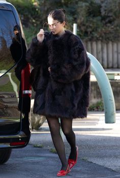 a woman in a black fur coat is getting out of a car and talking on the phone