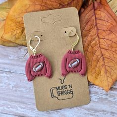 two pairs of pink knitted earrings on top of a wooden table next to leaves