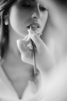 black and white photograph of a woman holding a flower in front of her face while brushing her teeth