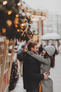 a man and woman embracing in front of a christmas tree with lights on the trees