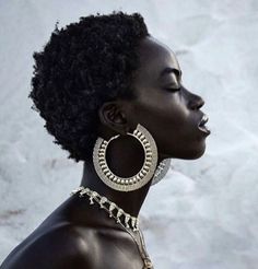 a woman with an afro haircut wearing gold earrings and a chain around her neck