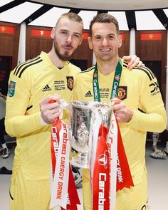 two men in yellow soccer uniforms holding a silver cup with red and white ribbons around their necks