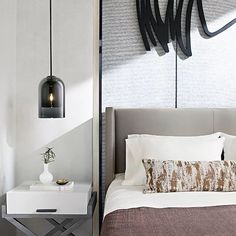 a bed with white sheets and pillows next to a wall mounted light fixture in a bedroom