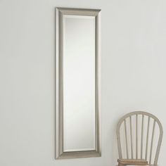 a white chair sitting next to a tall mirror on the side of a wall in a room