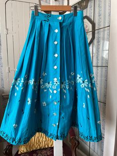 This cheerful skirt is made of crisp cotton in turquoise blue, with embossed/flocked flowers in white with black centres, stems and leaves. It fastens with buttons down the front. The measurements, taken with the skirt lying flat, are: waist, 12 1/2 inches; hips, 30 inches; length, 31 inches; bottom edge, 40+ inches. In very good condition. White And Black Flowers, Turquoise Skirt, Blue Pleated Skirt, Black Flowers, Vintage Turquoise, Historical Clothing, Full Skirt, Turquoise Blue, Pleated Skirt