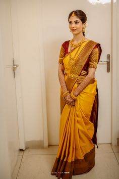 a woman in a yellow and brown sari standing next to a white door with her hands on her hips