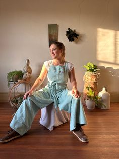 a woman sitting on top of a wooden floor next to a potted plant in a room