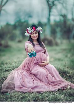 a pregnant woman in a pink dress sitting on the grass