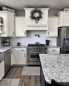 a kitchen with white cabinets and granite counter tops, stainless steel appliances and a wreath on the wall