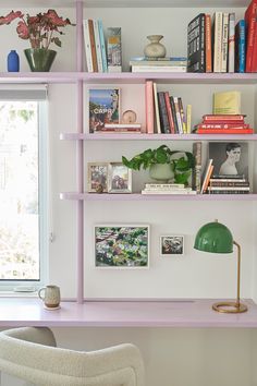 a white chair sitting in front of a purple book shelf filled with books and plants