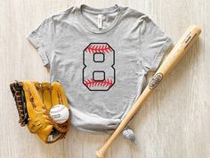 This personalized baseball number shirt is perfect for game day. Represent your favorite player by wearing a shirt with their number. This baseball number shirt makes a great gift for baseball moms. Get one for yourself or as a gift to someone special. PRODUCT DETAILS     - Bella Canvas 100% soft cotton t-shirt (polyester content varies with color)     - Light, breathable fabric     - Unisex fit - please refer to the size chart in the listing photos for most accurate measurement DESIGN AND PRINT Sporty Team Name Shirt For Baseball Season, Sporty Shirt With Team Name For Baseball Season, Sporty Pre-shrunk Shirt For Baseball Season, Baseball Season Team Shirt Fan Apparel, Baseball Season Fan Apparel Shirt With Team Name, Number Print T-shirt For Baseball Season, Pre-shrunk Shirt For College Baseball Season, Baseball Season Fan Gear Shirt With Team Spirit, Team Name Shirt For College Baseball Season