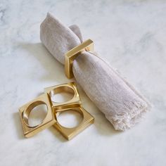 two gold napkin rings sitting next to each other on a marble counter top with a white towel