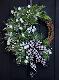 a wreath with white and green decorations hanging on a black front door for the holiday season