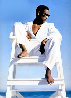 a man sitting on top of a white chair in front of the ocean with his legs crossed