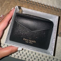 a hand holding a black card case in it's box with the name kate spade on it