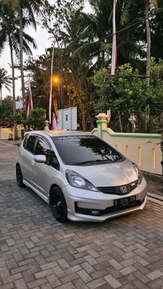 a silver car parked on the side of a brick road next to trees and flags