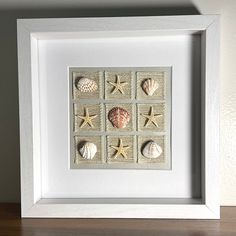 a white frame with seashells and starfish in it on a wooden table