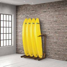 three yellow surfboards are on a rack in front of a brick wall and window