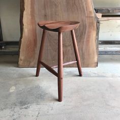 a wooden stool sitting on top of a cement floor next to a piece of wood