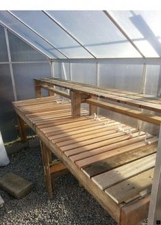 a bench made out of wooden pallets in a small greenhouse with glass walls and gravel flooring