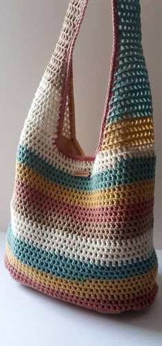 a crocheted purse is sitting on a table next to a white wall and it's handles are made out of multicolored yarn